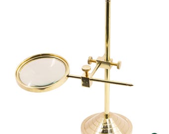 May include: A brass magnifying glass on a stand. The round lens is held by a brass frame and is adjustable. The stand has a round base and a vertical pole with adjustable knobs. The magnifying glass is a vintage style.