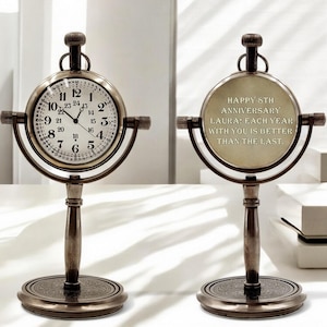 May include: A vintage-style desk clock with a round face and a bronze finish. The clock face displays black numerals on a white background. The back of the clock has the text: "HAPPY 5TH ANNIVERSARY LAURA: EACH YEAR WITH YOU IS BETTER THAN THE LAST."