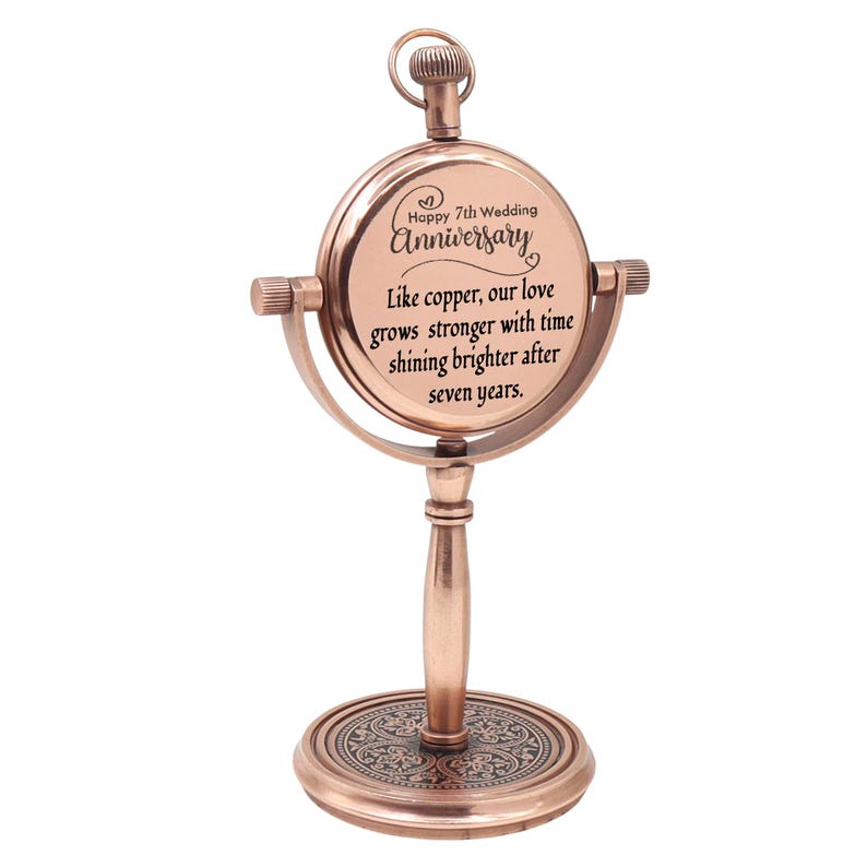 May include: A copper-toned metal desk clock with a circular frame mounted on a pedestal base. The clock face features the text: Happy 7th Wedding Anniversary, Like copper, our love grows stronger with time shining brighter after seven years.