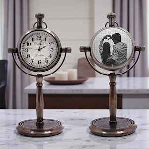 May include: Two antique-style pocket watch clocks with bronze-colored stands. One clock displays a traditional clock face with Roman numerals, while the other features a black and white photo of a couple making a heart shape with their hands.