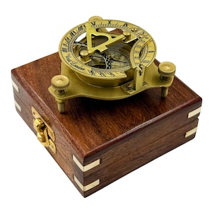 May include: A brass sundial compass with Roman numerals and the inscription West London, mounted on a square dark wood box featuring brass corner inlays and a front latch. The instrument includes an adjustable gnomon and levelling screws.