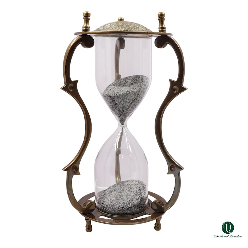 Puede incluir: Un reloj de arena con un bulbo de vidrio transparente lleno de arena gris, encerrado en un marco de metal color bronce oscuro con soportes curvos y una tapa texturizada. La base es circular con pies peque&ntilde;os, el logo Dollond London es visible.