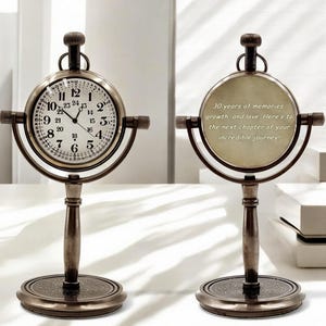 May include: Two antique-style bronze desk clocks on stands. One clock face features black numerals and hands with a 24-hour scale. The other side displays the engraved text: 30 years of memories, growth, and love. Here's to the next chapter of your incredible journey!