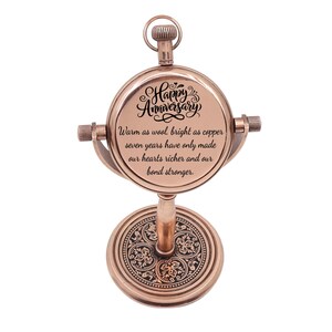 May include: A copper-colored metal desk clock with a circular face featuring the text Happy Anniversary, Warm as wool, bright as copper, seven years have only made our hearts richer and our bond stronger. The base has an intricate floral pattern.