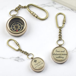May include: Three antique brass-toned metal keychains. One features a functional compass with a black face and gold cardinal directions. The other two are circular pendants with inscriptions: "Time and distance mean nothing" and "Together, we find the way."