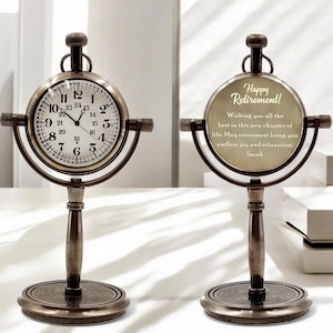 May include: Antique-style desk clock with a round face and Roman numerals. The clock has a bronze finish and a decorative base. The clock face displays the time, while the other side has the text "Happy Retirement!" and a retirement message.