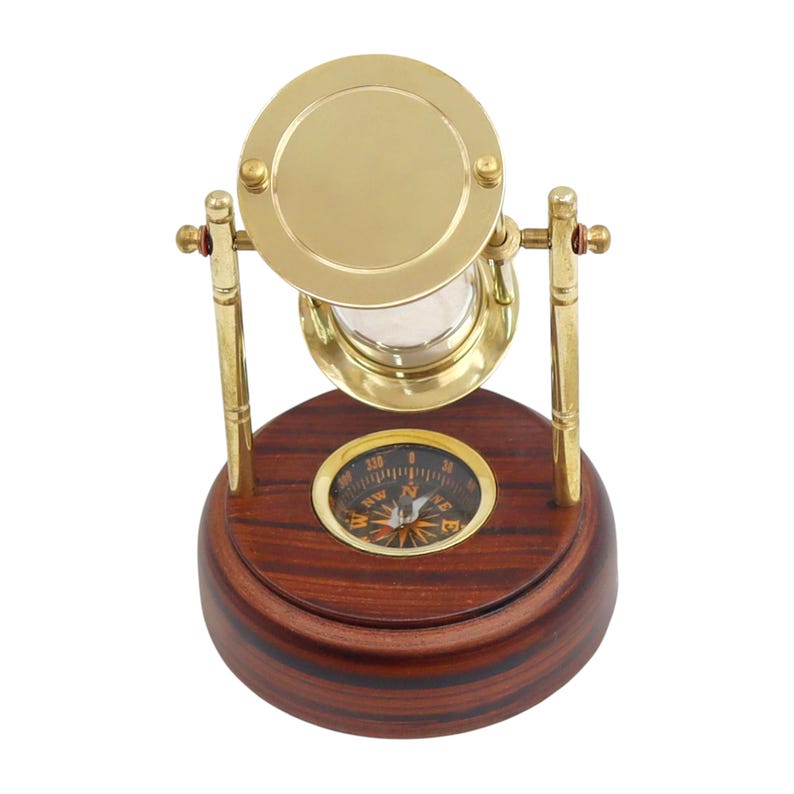 K&ouml;nnte beinhalten: Dekorative Sanduhr aus Messing und Glas mit Holzsockel und Kompass. Die Sanduhr ist ein klassisches Design, oft mit nautischen Themen verbunden. Der Holzsockel hat eine satte, dunkelbraune Farbe. Der Kompass ist in die Basis eingelassen.
