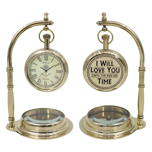 May include: Two brass-colored pocket watch displays. One shows a clock face with Roman numerals and the word "London". The other has the text "I WILL LOVE YOU UNTIL THE END OF TIME". Each watch is suspended from a curved stand.
