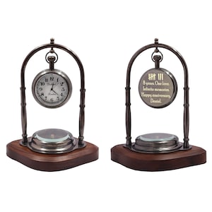 Op de afbeelding: Een klok in vintage-stijl met een donker metalen frame en een houten voet. De wijzerplaat toont Romeinse cijfers. De tweede wijzerplaat heeft de tekst "8 jaar. Eén liefde. Oneindige herinneringen. Fijne verjaardag, Daniel."