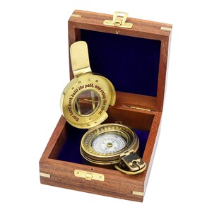 May include: A brass pocket compass with a hinged lid featuring the engraved text 'Your hard work built the path, now enjoy the view.' The compass rests inside a square wooden box with a dark blue velvet lining and gold-toned metal hardware.