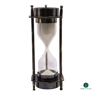 Peut inclure: Un sablier de style antique avec un centre en verre transparent et un cadre en métal bronze foncé. Le sablier contient du sable fin et clair. Le cadre a une base et un sommet rectangulaires, avec des supports verticaux et des ornements décoratifs.