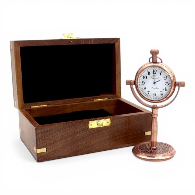 May include: A dark brown wooden box with a hinged lid and brass hardware, accompanied by a copper-toned desk clock on a pedestal stand. The clock features a white face with black Arabic numerals and the text "Dalton London" printed on it.