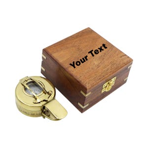 May include: A polished brass nautical compass with a hinged lid and a square wooden storage box featuring brass corner accents and a gold-toned latch. The lid of the wooden box is engraved with the black text Your Text.