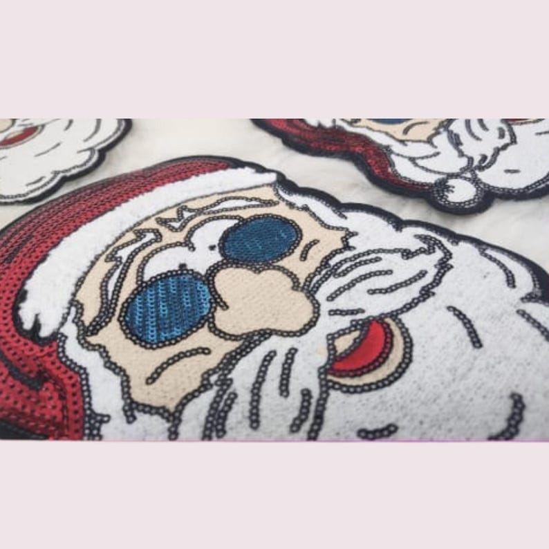 May include: Close-up of sequined Santa Claus face patches. The patches feature a red hat, white beard, and blue sequined eyes. The Santa face is outlined in black, with a beige face and red mouth.