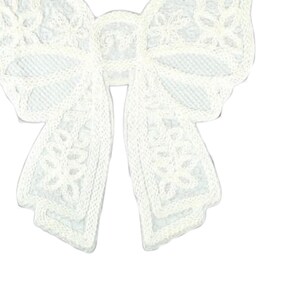 May include: A white lace bow with intricate floral patterns. The bow is made of a delicate, textured fabric and features a classic bow shape, perfect for embellishing crafts or adding a touch of elegance to accessories.