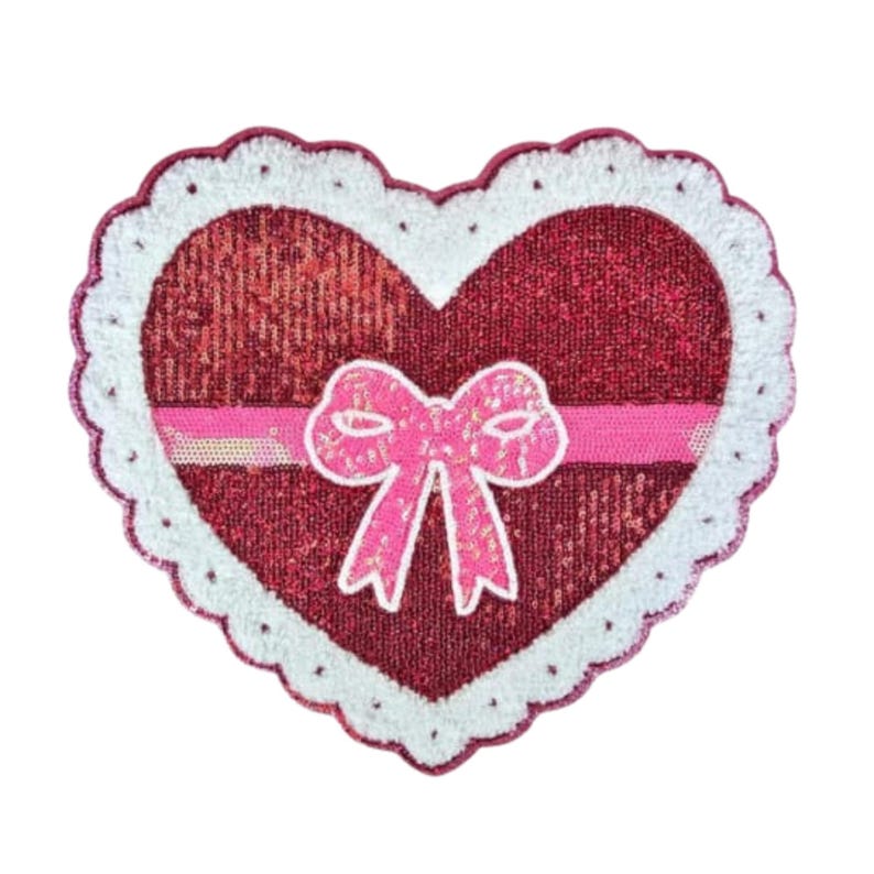 May include: A heart-shaped patch with a red sequined center, a white scalloped border, and a pink ribbon with a bow. The patch is designed with a Valentine's Day theme.