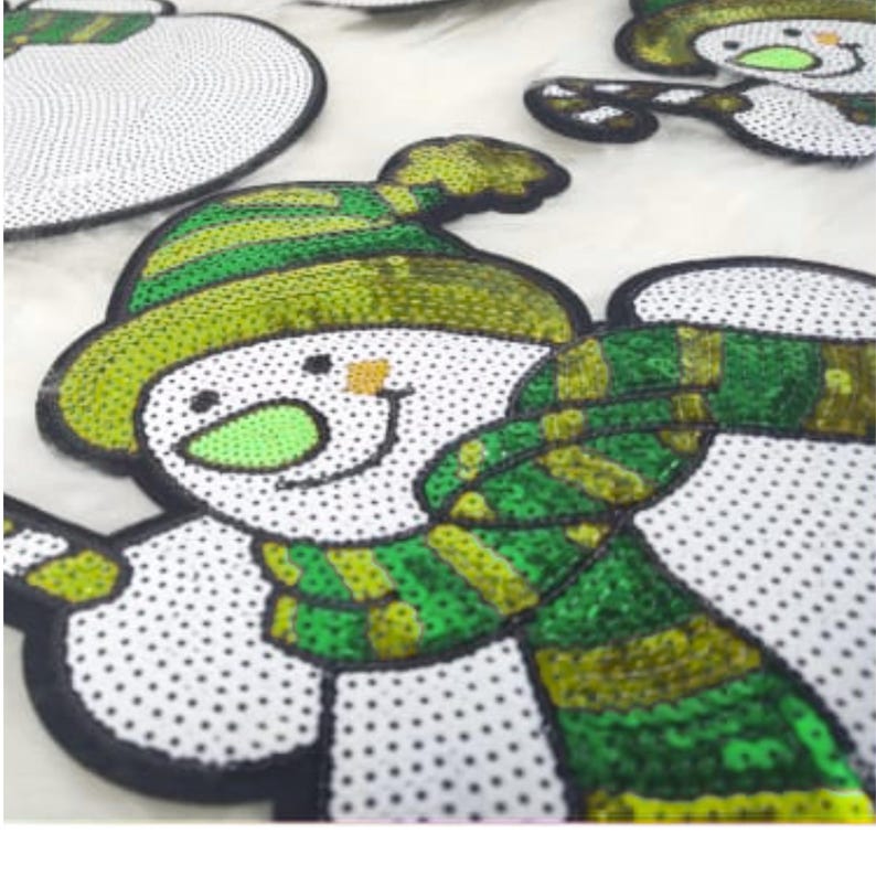 May include: Close-up of several snowman-shaped sequin patches. Each snowman has a white body with black polka dots, a green and yellow hat and scarf, and a smiling face. The patches are likely for holiday crafts.