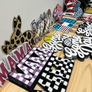 Könnte beinhalten: Eine Sammlung dekorativer Aufnäher in verschiedenen Formen und Designs. Enthält einen Hasen mit Leopardenmuster, Baseball-Aufnäher, Aufnäher mit der Aufschrift "Mama" und Schachbrettmuster. Weitere Aufnäher zeigen Eis am Stiel- und Flaggen-Designs.