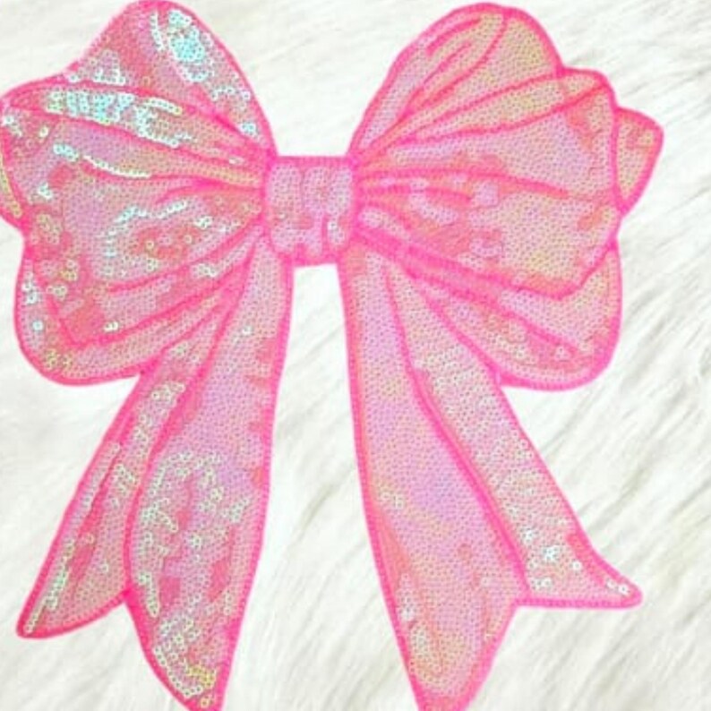 May include: A large, pink sequined bow with a shimmering, iridescent effect. The bow is a bright, eye-catching accessory, perfect for embellishing clothing, gifts, or crafts. The bow's design features multiple loops and long, flowing tails.