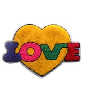 May include: A colorful patch featuring the word "LOVE" over a yellow heart. The letters are in purple, pink, green, and red, with a white border. The patch has a textured, fuzzy appearance.