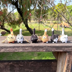 May include: A collection of six handmade crochet cat keychains in various colors, including yellow, gray, black, and orange. Each keychain features a gold-colored ring and a detailed cat design, perfect for cat lovers.