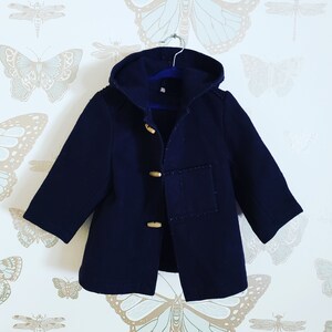 May include: A navy blue hooded coat with a toggle closure and a patch pocket on the front. The coat is hanging on a hanger against a white background with a butterfly pattern.