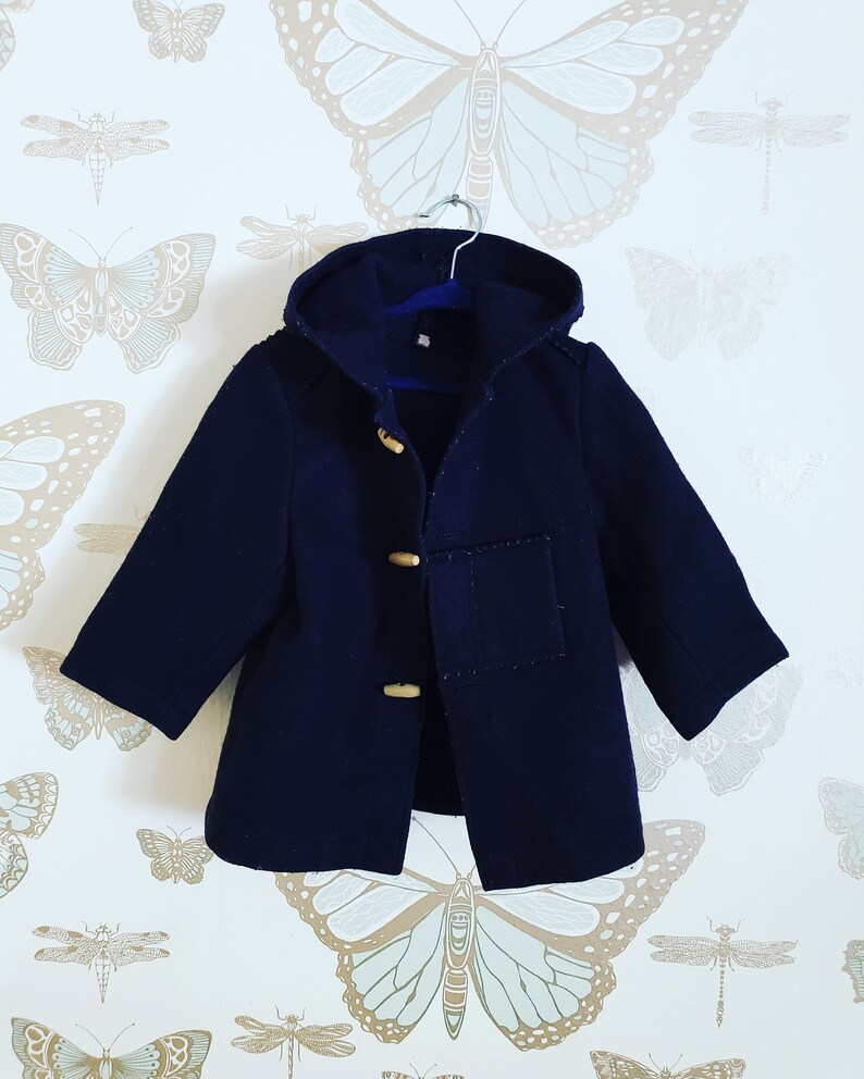 May include: A navy blue hooded coat with a toggle closure and a patch pocket on the front. The coat is hanging on a hanger against a white background with a butterfly pattern.