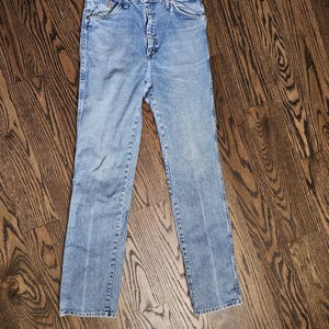 May include: Light blue denim jeans with a button and zipper closure. The jeans have front and back pockets, belt loops, and a straight leg design. The denim has a faded appearance.