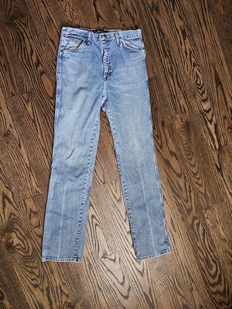 May include: Light blue denim jeans with a button and zipper closure. The jeans have front and back pockets, belt loops, and a straight leg design. The denim has a faded appearance.