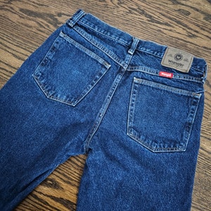 May include: A pair of blue denim jeans with a brown leather Wrangler label on the back pocket. The label has the text "Premium Quality" and a capital "W" inside a circle.