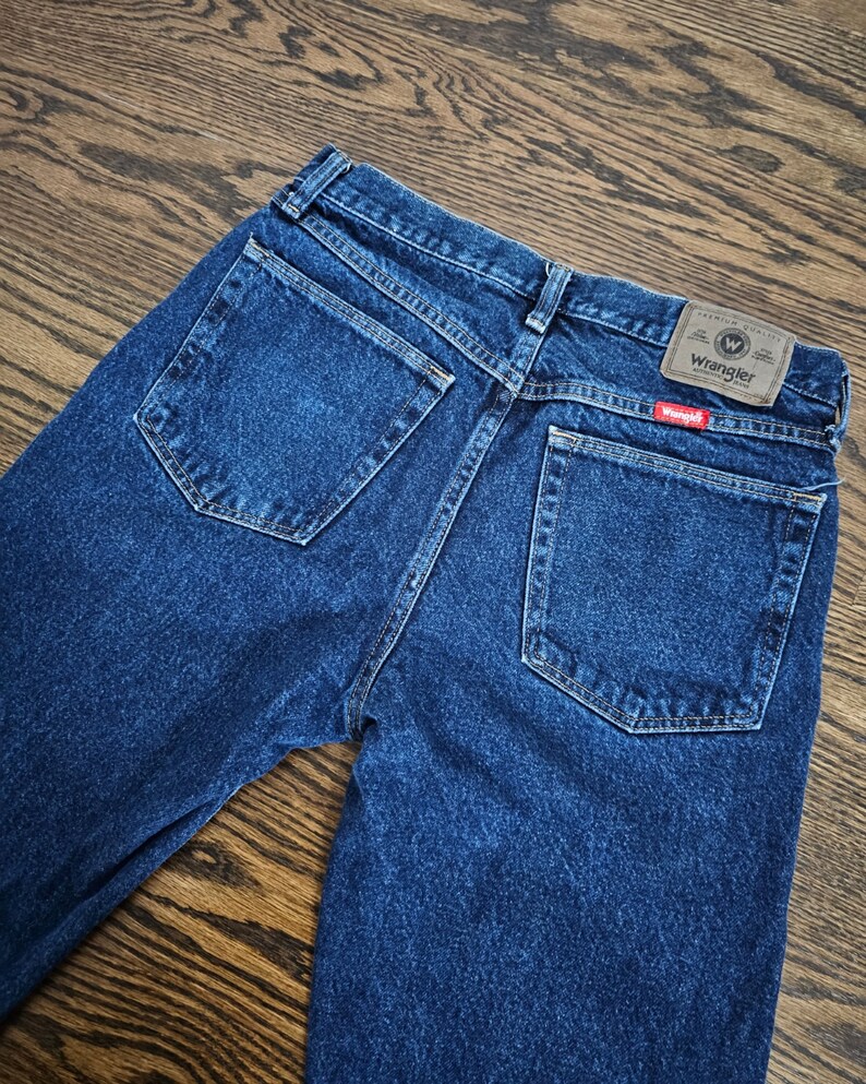May include: A pair of blue denim jeans with a brown leather Wrangler label on the back pocket. The label has the text "Premium Quality" and a capital "W" inside a circle.