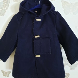 May include: A navy blue hooded coat with wooden toggle closures. The coat has a patch pocket on the front and a lined hood.