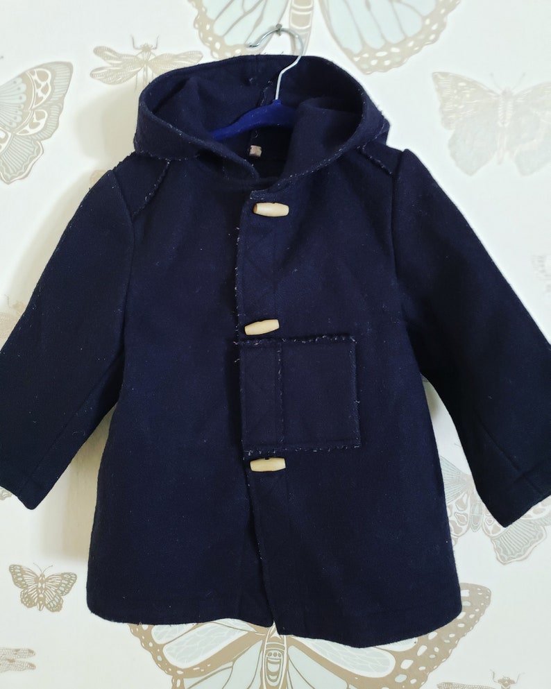 May include: A navy blue hooded coat with wooden toggle closures. The coat has a patch pocket on the front and a lined hood.