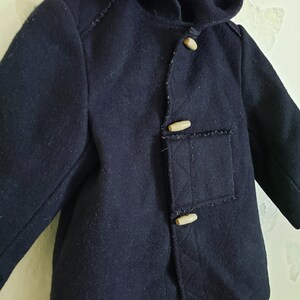May include: A dark blue hooded coat with a toggle closure and two pockets. The coat has a textured fabric and is made of wool.