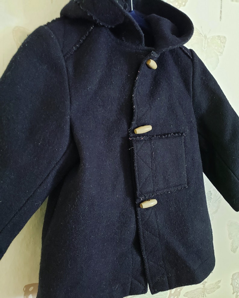 May include: A dark blue hooded coat with a toggle closure and two pockets. The coat has a textured fabric and is made of wool.