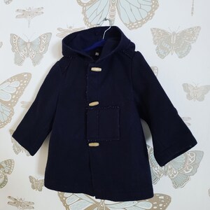 May include: A navy blue hooded coat with wooden toggle closures. The coat has a patch pocket on the left side and is hanging on a hanger.