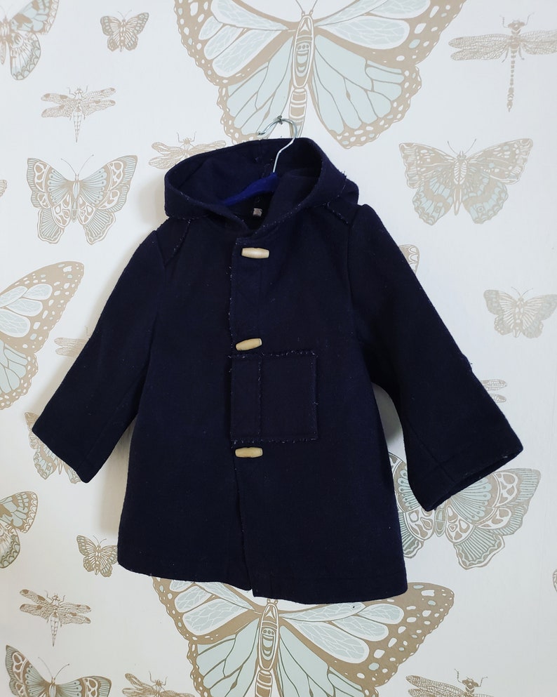 May include: A navy blue hooded coat with wooden toggle closures. The coat has a patch pocket on the left side and is hanging on a hanger.