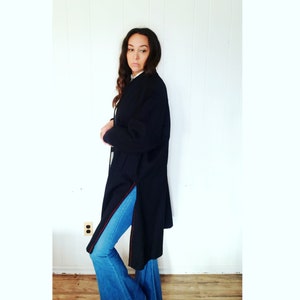 May include: A long black coat with red stitching on the sides. The coat is worn over blue jeans.