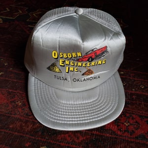May include: A silver and black mesh trucker hat with a yellow and black logo that says "Osborn Engineering Inc. Tulsa, Oklahoma". The logo also features a red car and piles of dirt.