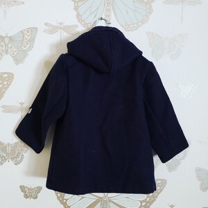 May include: A navy blue hooded coat with a zipper closure and a buttoned front. The coat has long sleeves and a relaxed fit.