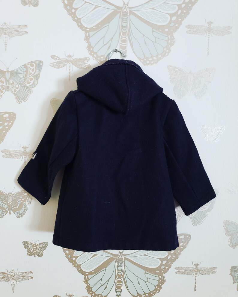 May include: A navy blue hooded coat with a zipper closure and a buttoned front. The coat has long sleeves and a relaxed fit.