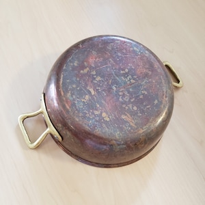 May include: A copper pot with brass handles. The pot has a patina finish and is showing signs of age.