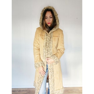 May include: A long, tan suede coat with a faux fur hood and trim. The coat has a zipper closure and pockets.