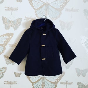 May include: A navy blue hooded coat with wooden toggle closures and a patch pocket on the front. The coat is hanging on a hanger against a white background with a butterfly pattern.