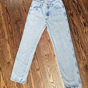 May include: Light blue denim jeans with a classic five-pocket design. The jeans have a straight leg cut and a faded wash, giving them a vintage look. The jeans are made of durable denim material.