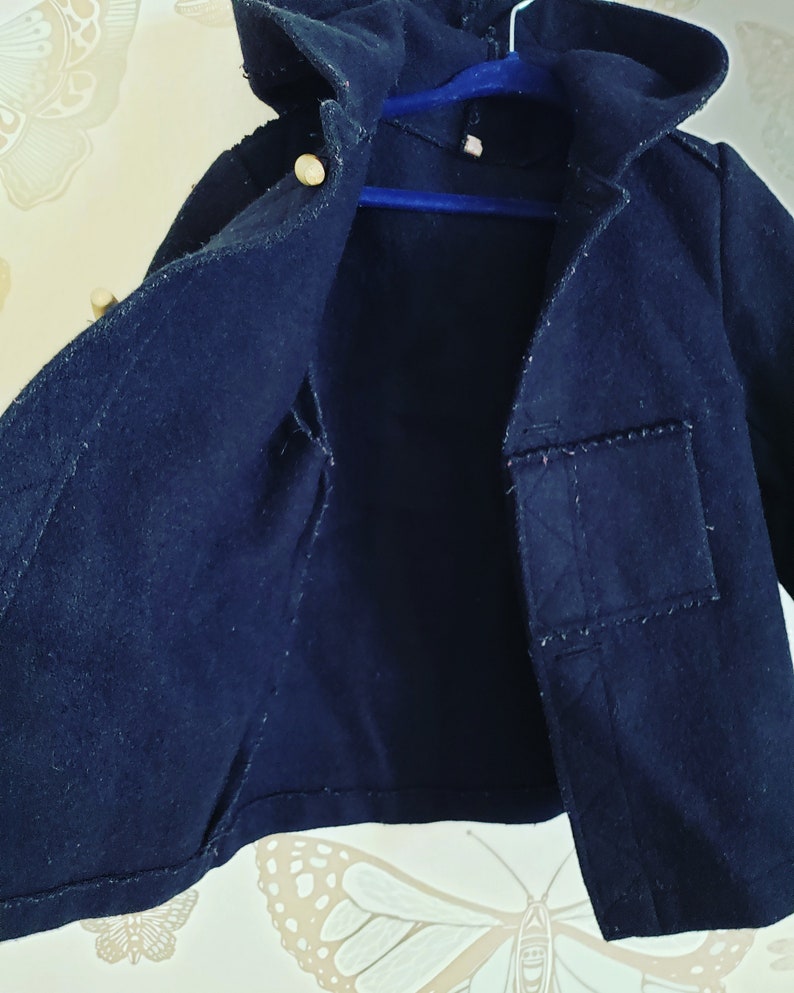 May include: A black hooded jacket with a small pocket on the right side. The jacket is unbuttoned and the inside is visible.