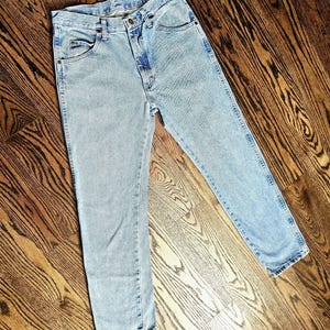 May include: Light blue denim jeans with a classic five-pocket design. The jeans have a straight leg cut and a button and zipper closure. The denim has a faded wash, giving them a vintage look.