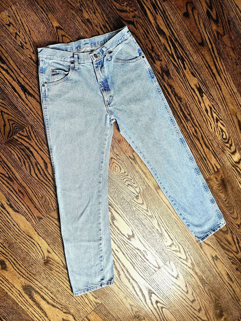 May include: Light blue denim jeans with a classic five-pocket design. The jeans have a straight leg cut and a button and zipper closure. The denim has a faded wash, giving them a vintage look.