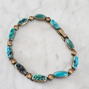 May include: A turquoise and green bracelet with carved floral accents and clear rhinestones. The bracelet is made of metal and has a clasp closure.
