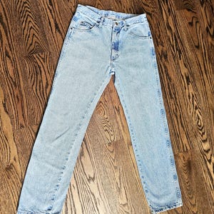 May include: Light blue denim jeans with a classic five-pocket design. The jeans have a straight leg cut and a button and zipper closure. The denim has a faded wash, giving them a vintage look.